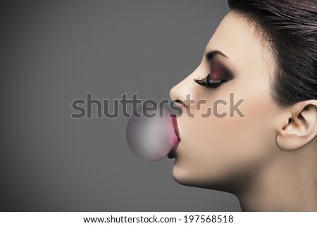 Beauty young woman makes a balloon with a bubble gum, grey background with copyspace