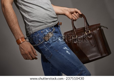 Young man carrying a leather bag against grey background