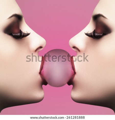 Sexy young woman makes a balloon with a bubble gum against pink background