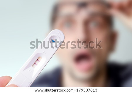 Positive pregnancy test held by a surprised man in the background