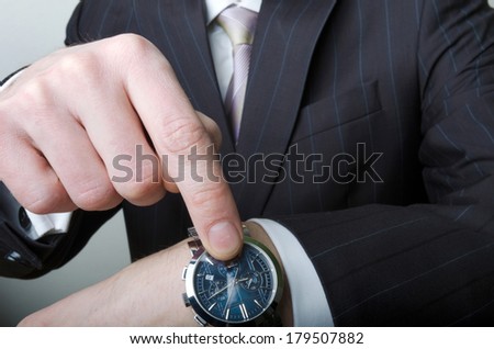A man in a suit, a white shirt and a tie pointing at his watch
