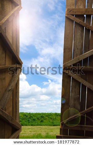 An open gate of a barn with a view of the sky and grass