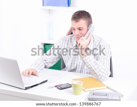 Young and handsome businessman in his office working on the laptop and making telephone conversation