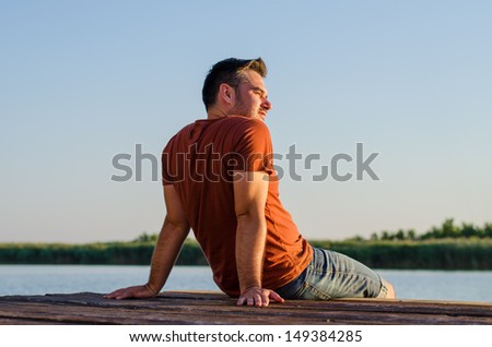 Young man sitting relaxing and enjoying the view of beautiful nature on the river dock