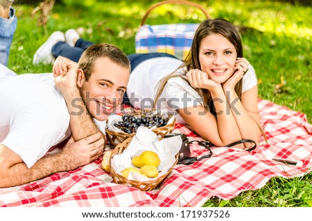 Happy young couple having a picnic and laying on the picnic cloth enjoying the autumn nature in the park
