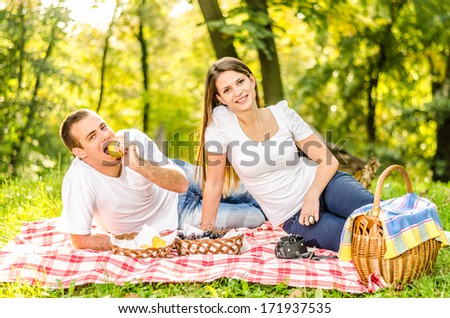 Happy young couple having a picnic and sitting on the picnic cloth enjoying the autumn nature in the park