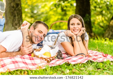 Happy young couple having a picnic and laying on the picnic cloth enjoying the autumn nature in the park