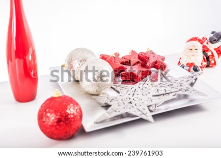 Red and silver christmas balls and stars on a silver decoration tray with a red and white decoration vases on a white background
