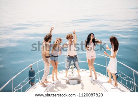Luxury vacation. Joyful young male and female friends dancing and having fun on a bow of sailing boat deck, smiling, hugging over amazing blue marine background with copyspace. Banner.