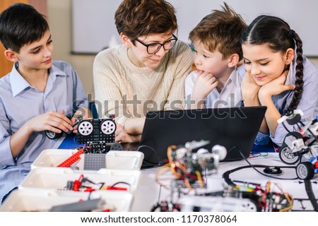 Team of little curious technicians working together with their teacher in robotics class