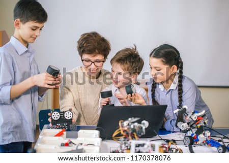 Curious smart caucasian pupils kids with female teacher enjoying science robotics lessons in technical school using laptop, study programming skill