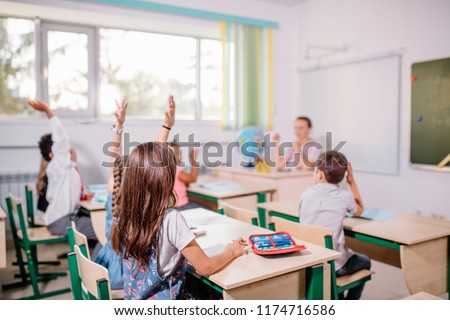 education, school, teaching, learning concept - group of schoolchildrens raising hands and teacher in classroom
