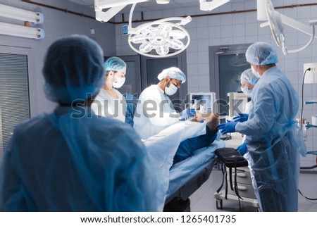 Photo of anesthesiologist with mask preparing patient to the surgery in modern operation theatre