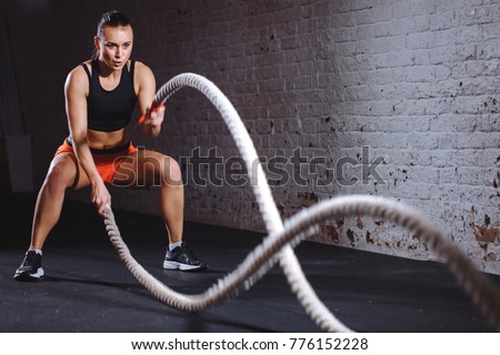 Woman training with battle rope in cross fit gym