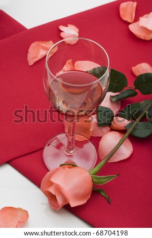 glass of red wine with red table cloth and pink rose on on white background.