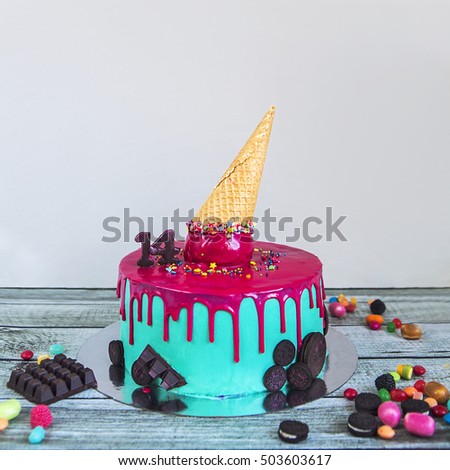 Birthday cake with pink turquoise coated with ice cream horn and candies on a wooden table.