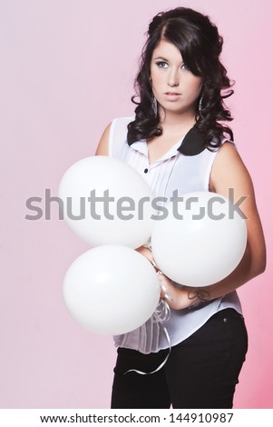 Caucasian teenage female posing in a white blouse and black jeans with a pink background holding three balloons
