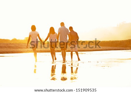 Family Of Four Silhouette By A Sunset Walking At The Beach