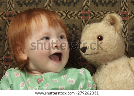 Antique teddy bear whispers secrets to a cute toddler.