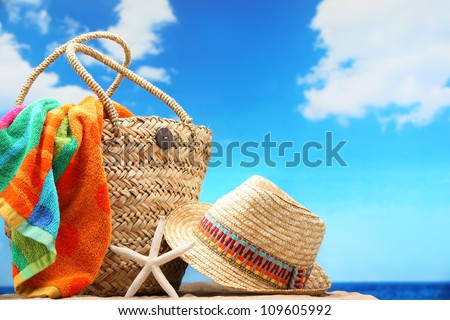 Closeup of summer beach bag and straw hat on sandy beach.