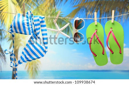 Women\'s swimsuit, sunglasses and flip-flops hanging on a rope near beach.