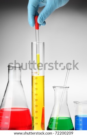 hand holding Pipette with emerging drop of liquid over graduated cylinder.