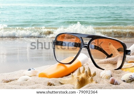 Sun glasses and bottle of balm solar on sandy beach.