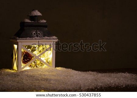 Pretty glowing Christmas lantern in fresh winter snow against a dark night background with copy space for your holiday message