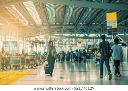 Traveling concept. Travelers asian woman walking with a luggage at airport terminal and airport terminal blurred crowd of travelling people on the background. (vintage color tone, advertise concept)