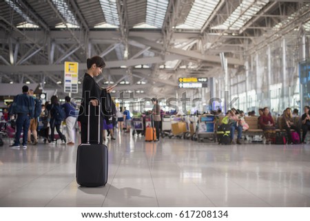 Elegant asian businesswoman checking e-mail on mobile phone with suitcase in airport and airport terminal blurred crowd of travelling people on the background.