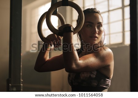 Exercising woman holding gymnast rings and looking away. Female taking rest after intense dip ring workout at gym.