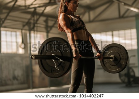 Determined and strong fitness woman training with heavy weights in fitness club. Female athlete holding heavy weight barbell in gym.