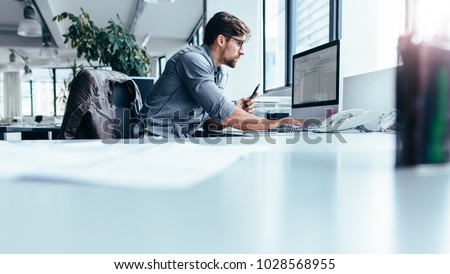 Young man sitting in office and working on desktop pc. Businessman looking at computer monitor while working in office.