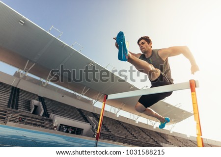 Close up of a runner jumping over an hurdle during track and field event. Athlete running a hurdle race in a stadium.