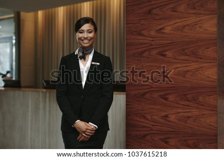 Portrait of happy female hotel receptionist standing at workplace. Smiling woman receptionist working in hotel.