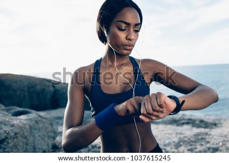 Fit female runner using smart watch to monitor her performance. African Woman setting fitness app on her smartwatch before running session.