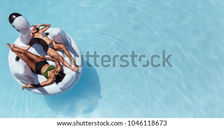 Top view of female friends wearing bikini lying on an inflatable toy in pool. Woman sunbathing on floating pool inflatable toy.