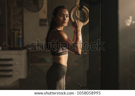 Fit woman holding gymnast rings at the gym. Young female exercising at gym.