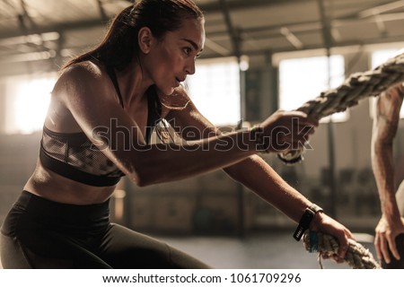 Fit woman using battle ropes during strength training at the gym. Athlete moving the ropes for burning fats at health club.
