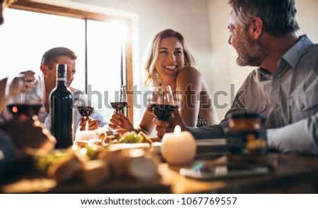 Smiling woman talking with friends sitting at dining tablet at home. Group of people having great time at dinner party.