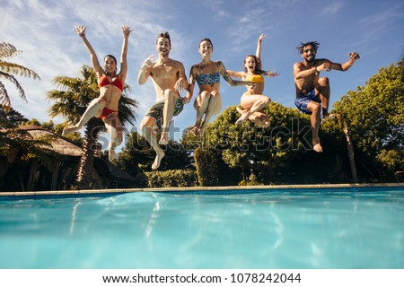Group of crazy young people jumping into a swimming pool. Friends having fun at a holiday resort.