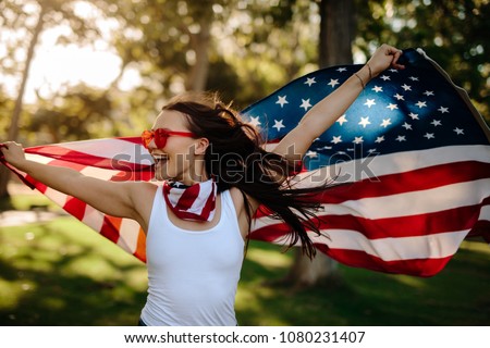 Young woman enjoying in park holding USA flag. American girl with national flag having fun at the park.