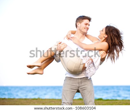 Portrait of a guy carrying his beautiful girlfriend in a windy beach
