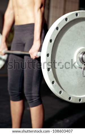 Closeup of heavy weight bar with woman performing deadlift in background