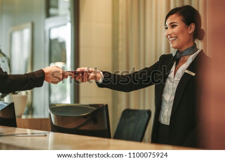 Smiling receptionist behind the hotel counter attending female guest. Concierge giving the documents to hotel guest.