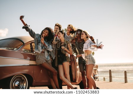 Diverse friends on road trip taking selfie with mobile phone. Group of men and women taking self portrait outdoors by the car.