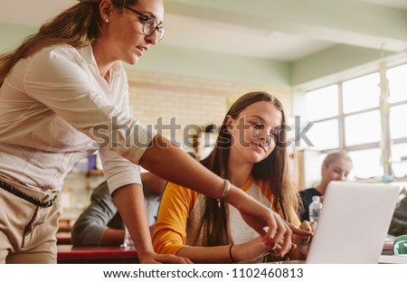 Teacher helping student in classroom. Lecturer pointing at laptop screen and showing something to female student.