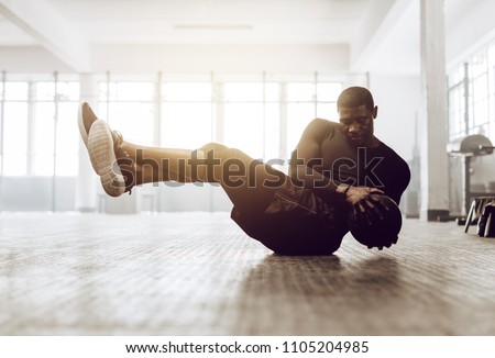 Athletic man doing abdomen exercise on the floor. Man doing workout using a medicine ball at the gym.