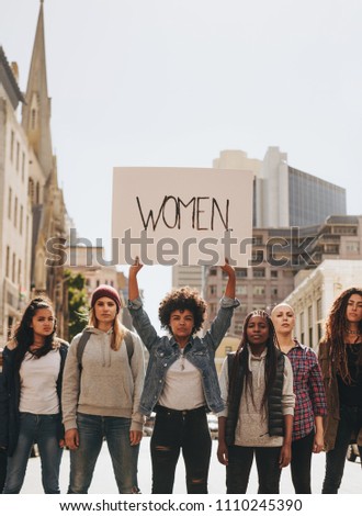 Multi-ethnic group of females protesting for women empowerment outdoors on road. Young african female with group holding banner sign during a protest.