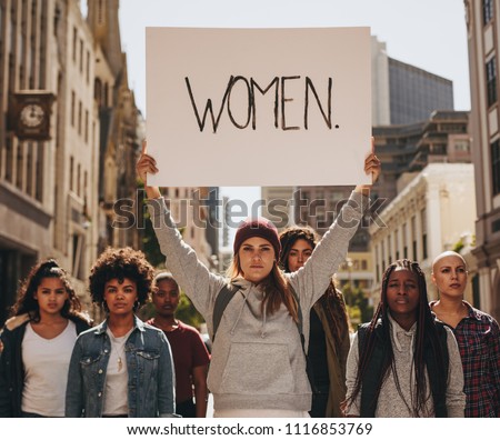 Group of females protesters marching on the road with signboard of women. Woman holding a protest sign about women empowerment with group of females around.